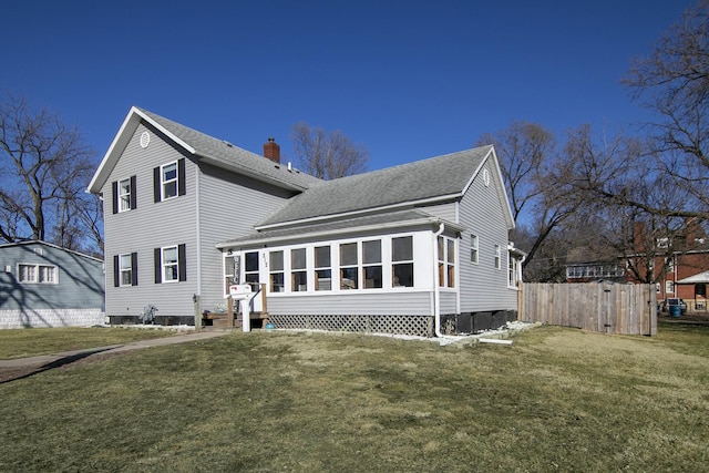 rear view of property with roof with shingles, a chimney, a lawn, a sunroom, and fence