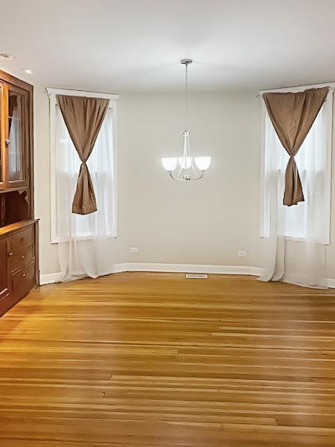 unfurnished dining area with baseboards, visible vents, light wood finished floors, and an inviting chandelier