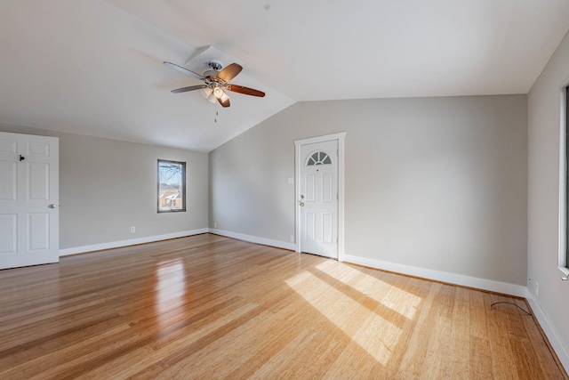 empty room with vaulted ceiling, ceiling fan, baseboards, and light wood-style floors