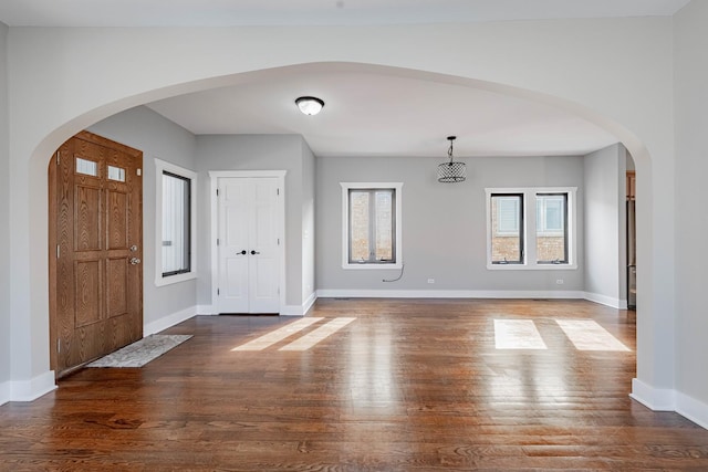 entrance foyer with baseboards, arched walkways, and wood finished floors