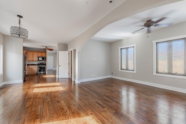 unfurnished living room featuring arched walkways, dark wood finished floors, and baseboards