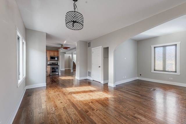 unfurnished living room with arched walkways, dark wood-style flooring, stairway, and visible vents