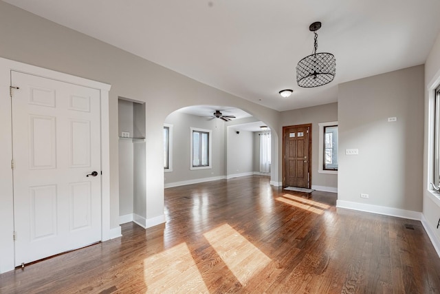 foyer featuring dark wood-style floors, baseboards, visible vents, and arched walkways