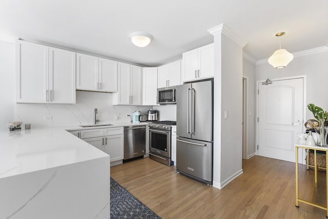 kitchen featuring high quality appliances, wood finished floors, light stone countertops, crown molding, and a sink