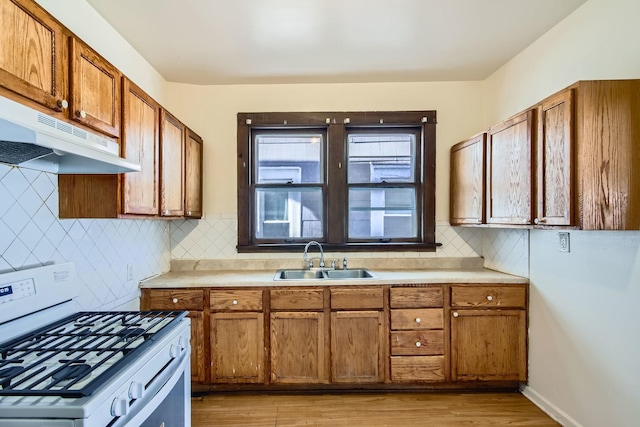 kitchen with brown cabinets, light countertops, white gas stove, under cabinet range hood, and a sink