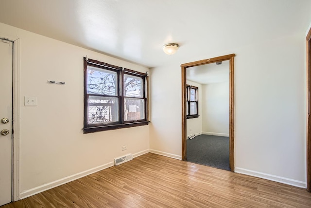 spare room featuring light wood finished floors, baseboards, and visible vents