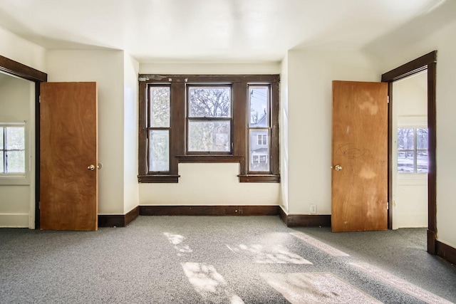 unfurnished bedroom featuring dark colored carpet, multiple windows, and baseboards