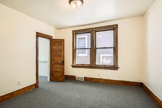 spare room featuring dark colored carpet, visible vents, and baseboards