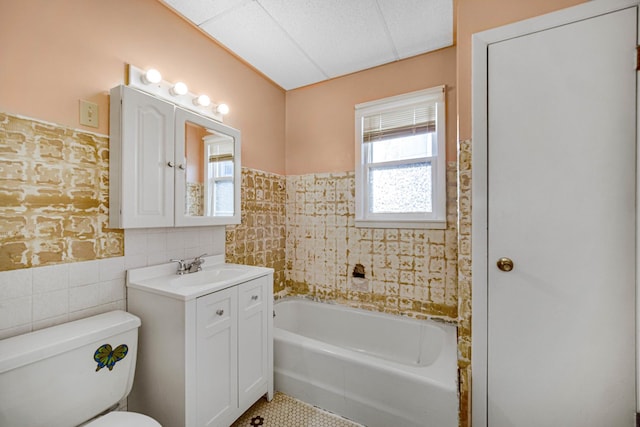 full bathroom with wainscoting, toilet, a washtub, vanity, and tile walls