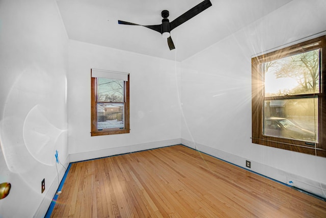 empty room featuring ceiling fan, baseboards, wood finished floors, and a healthy amount of sunlight