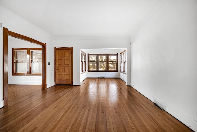 unfurnished living room featuring crown molding, baseboards, and wood finished floors