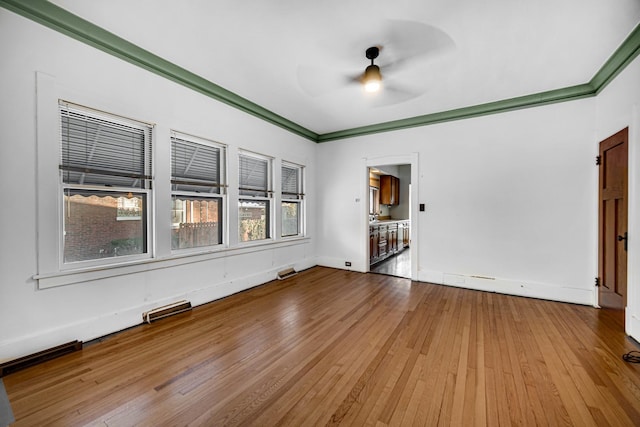 empty room featuring light wood finished floors, baseboards, ornamental molding, and a ceiling fan