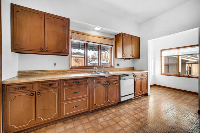 kitchen with brown cabinetry, light countertops, a sink, and dishwashing machine