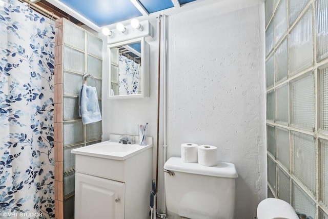 bathroom with a textured wall, a shower with shower curtain, vanity, and toilet