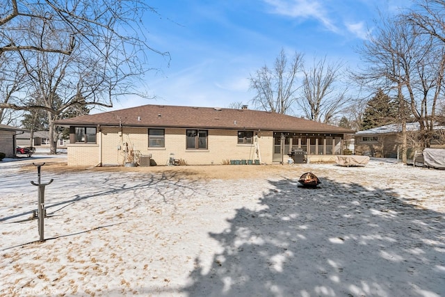 snow covered property with a sunroom, central AC unit, and brick siding