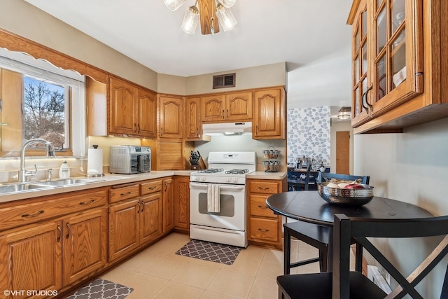 kitchen featuring under cabinet range hood, white range with gas stovetop, a sink, light countertops, and glass insert cabinets