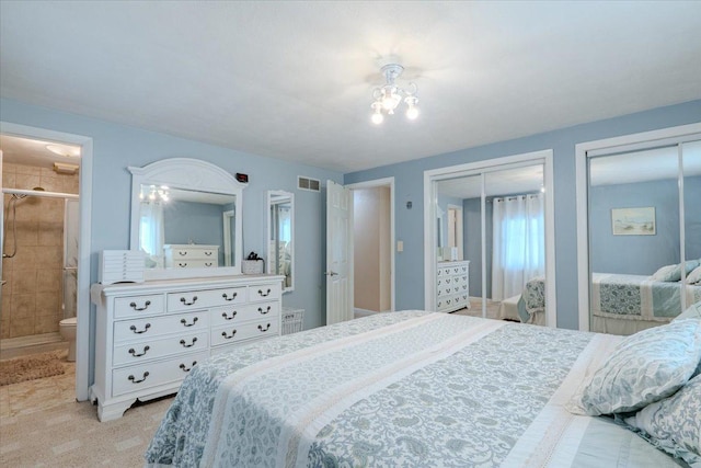 bedroom with visible vents, connected bathroom, light carpet, and two closets