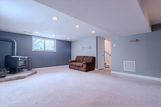 sitting room featuring light colored carpet, visible vents, a wood stove, baseboards, and stairs