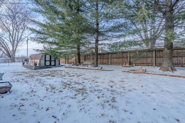 yard layered in snow with an outbuilding, a storage shed, and a fenced backyard