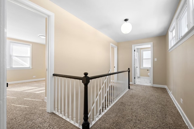 hallway with carpet floors, an upstairs landing, and baseboards