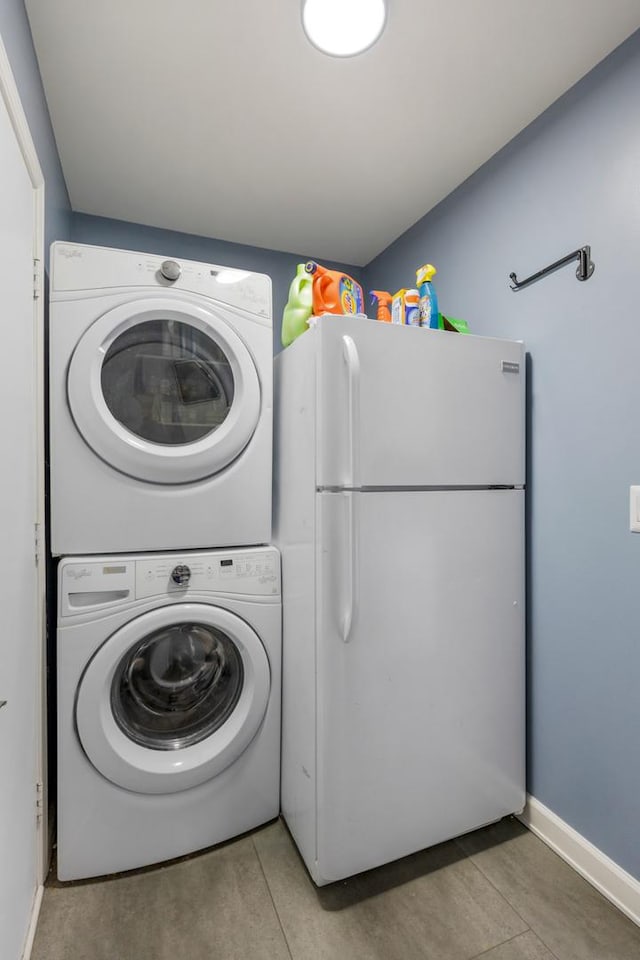 laundry area featuring light tile patterned floors, laundry area, stacked washing maching and dryer, and baseboards