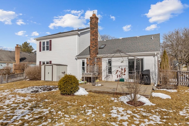 snow covered property with a chimney, fence, a deck, a shed, and an outdoor structure