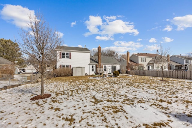 snow covered back of property with a storage shed, a residential view, fence, and an outbuilding