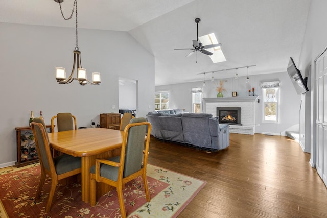 dining room with baseboards, lofted ceiling with skylight, dark wood-style flooring, a fireplace, and ceiling fan with notable chandelier