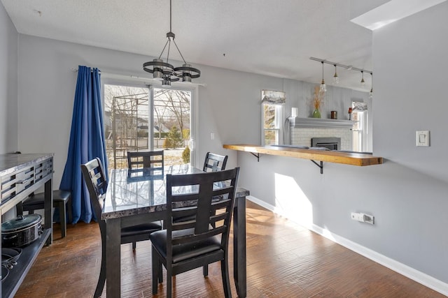 dining area with a fireplace, dark wood finished floors, a notable chandelier, a textured ceiling, and baseboards