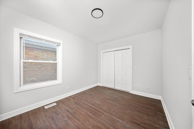 unfurnished bedroom featuring visible vents, baseboards, dark wood finished floors, and a closet