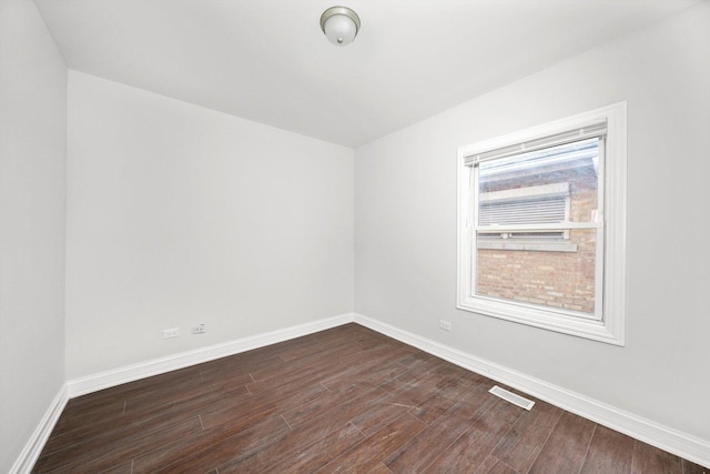 spare room featuring dark wood-type flooring, visible vents, and baseboards