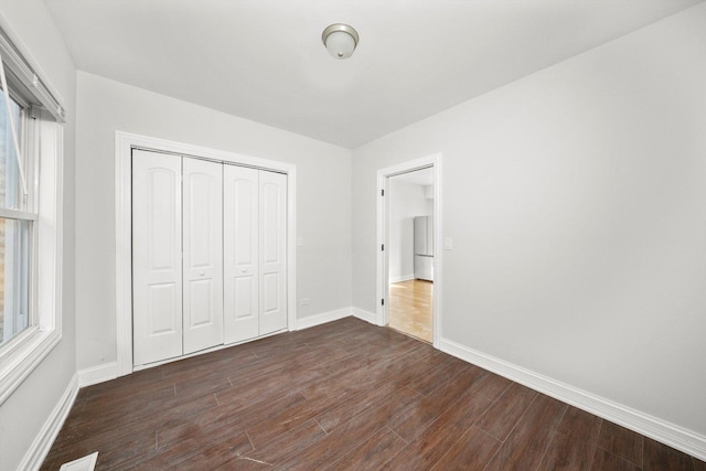 unfurnished bedroom featuring dark wood-style floors, a closet, visible vents, and baseboards