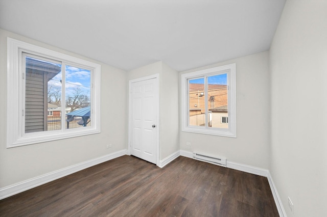 unfurnished bedroom with dark wood-style floors, multiple windows, baseboard heating, and baseboards