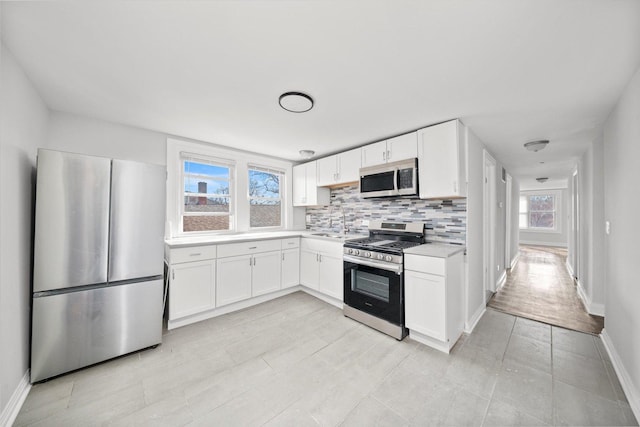 kitchen with baseboards, decorative backsplash, stainless steel appliances, light countertops, and white cabinetry