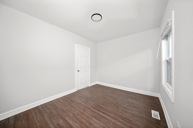 spare room featuring dark wood-style flooring, visible vents, and baseboards