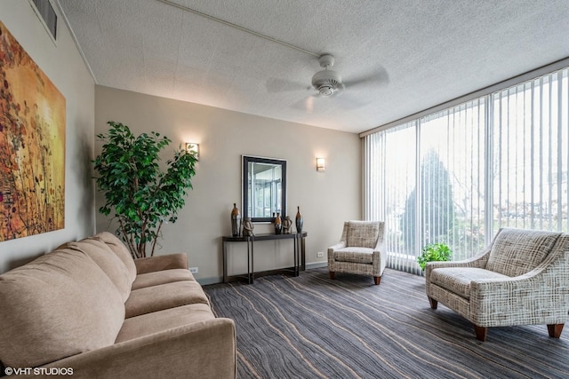 living area featuring ceiling fan, visible vents, baseboards, floor to ceiling windows, and dark carpet