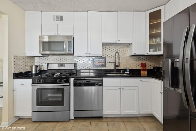 kitchen featuring visible vents, dark countertops, glass insert cabinets, stainless steel appliances, and a sink