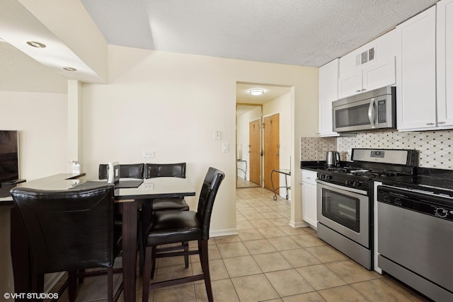 kitchen with light tile patterned floors, stainless steel appliances, dark countertops, backsplash, and white cabinetry