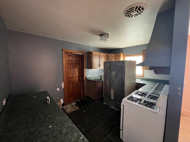 kitchen with visible vents, white range with gas cooktop, backsplash, freestanding refrigerator, and dark countertops