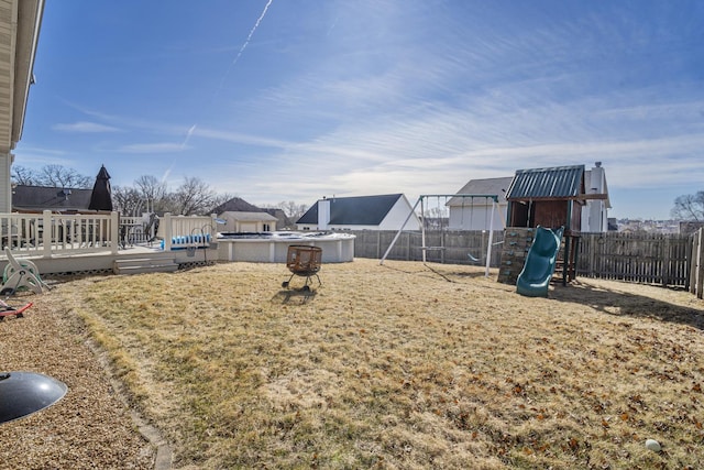 view of yard featuring a playground, a fenced backyard, a wooden deck, and a fenced in pool