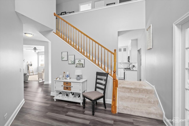 staircase featuring a ceiling fan, a high ceiling, baseboards, and wood finished floors