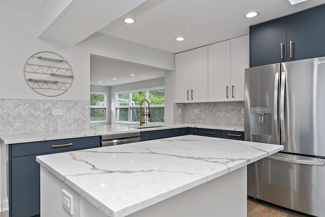 kitchen with a kitchen island, light stone counters, stainless steel appliances, blue cabinetry, and a sink