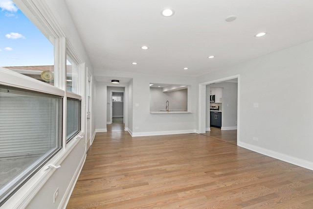 unfurnished living room with baseboards, a sink, light wood-style flooring, and recessed lighting