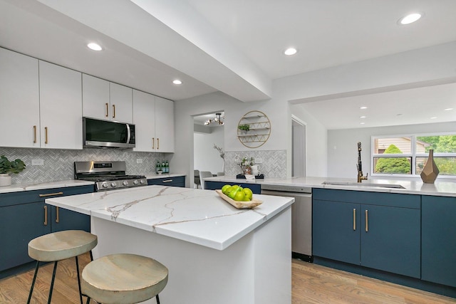 kitchen featuring white cabinets, a kitchen island, appliances with stainless steel finishes, blue cabinetry, and a sink