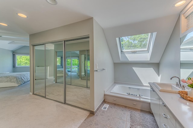 ensuite bathroom with vaulted ceiling with skylight, connected bathroom, vanity, visible vents, and a bath