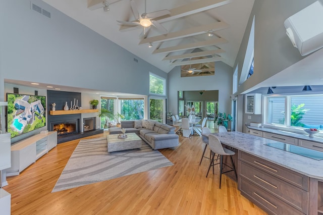 living area featuring a warm lit fireplace, light wood finished floors, ceiling fan, and visible vents