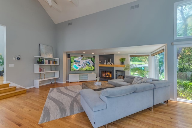 living area featuring a large fireplace, high vaulted ceiling, visible vents, and light wood-style flooring