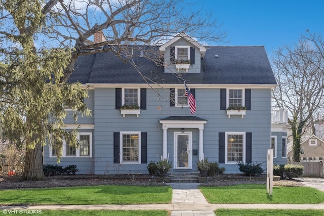 view of front facade featuring a chimney, roof with shingles, and a front yard