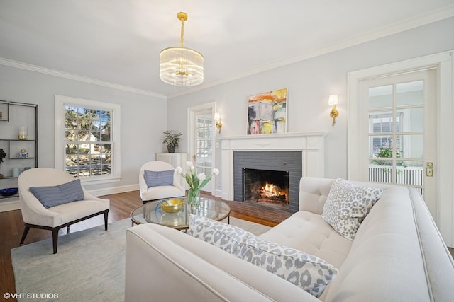 living room with a notable chandelier, a fireplace, wood finished floors, baseboards, and ornamental molding