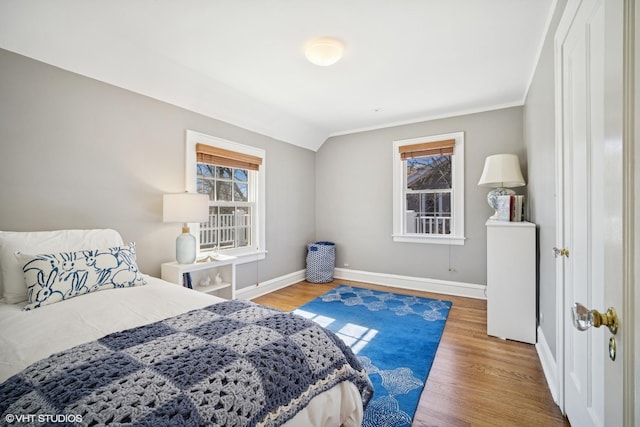 bedroom featuring vaulted ceiling, multiple windows, wood finished floors, and baseboards